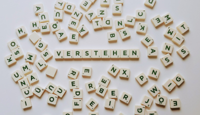Mit Scrabble Steinen liegt im Zentrum das Wort Verstehen. Darum herum liegen verschiedene Scrabble Steine durcheinander.