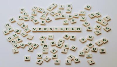Scrabble-Steine liegen auf einer weißen Fläche wild durcheinander. In der Mitte liegt das Wort VERSTEHEN.