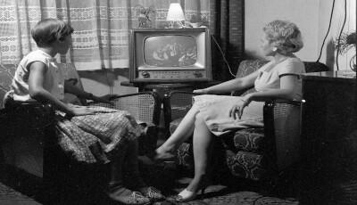 Zwei Frauen sitzen vor einem kleinen Röhrenfernseher. Das Schwarzweißbild ist eine historische Aufnahme.