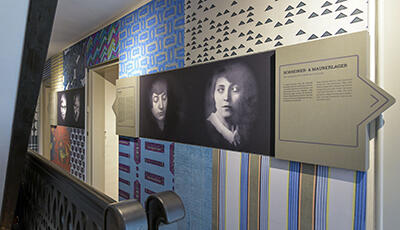 Blick in das Treppenhaus des Marieluise-Fleißer-Hauses mit farbiger Tapete sowie Bild- und Texttafeln zur Person Marieluise Fleißer.