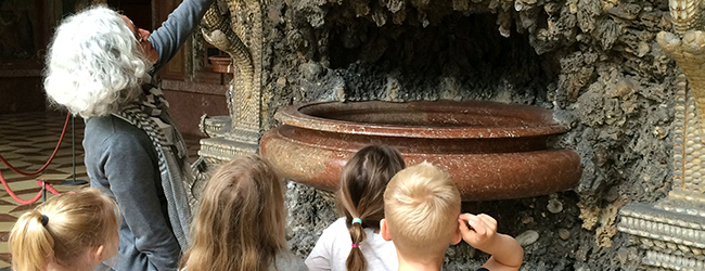 Eine erwachsene Personen und mehrere Kinder vor einem Objekt im Museum.
