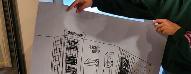 Zwei Hände halten ein Plakat, auf dem der Aufbau einer Ausstellungsabteilung skizziert wurde.